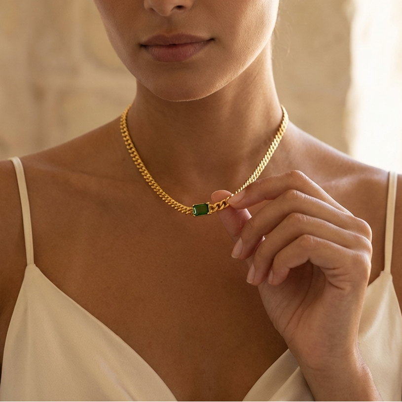 Woman wearing a gold necklace with a green gemstone against a neutral background