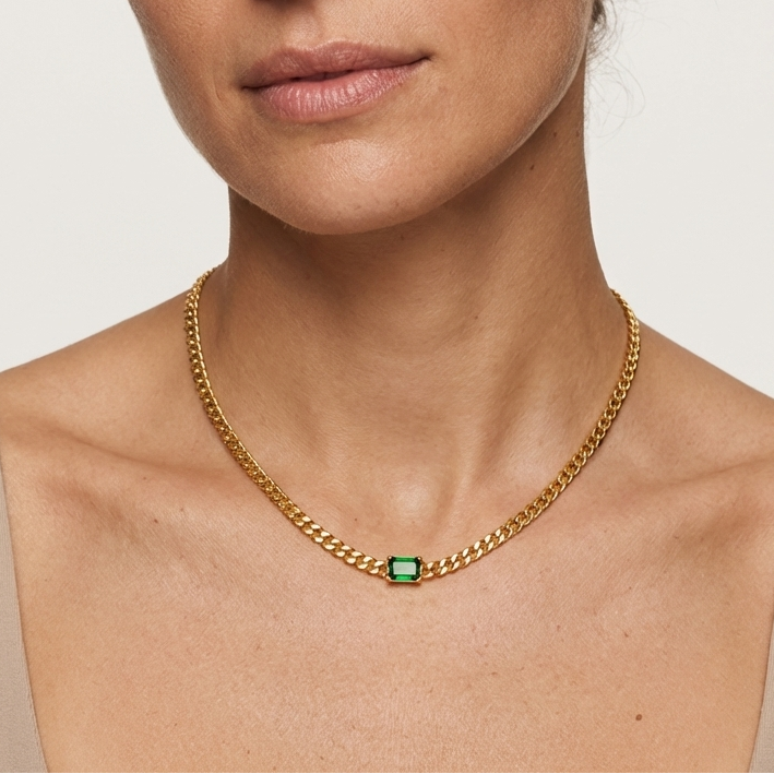 Woman wearing a gold chain necklace with a green gemstone on a plain background