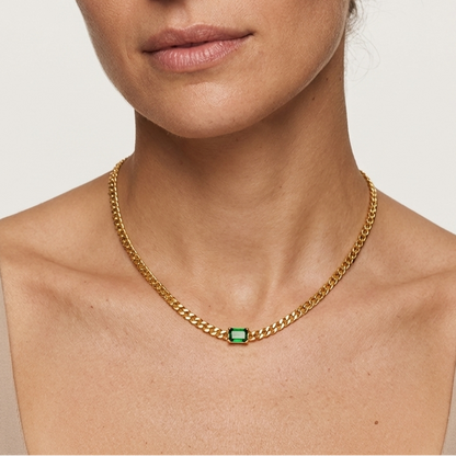 Woman wearing a gold chain necklace with a green gemstone on a plain background