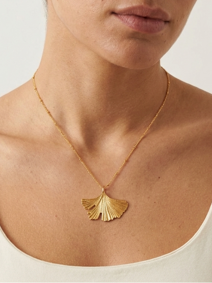 Woman wearing a gold necklace with a leaf pendant on a plain background