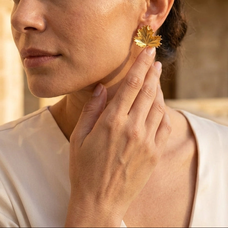 Woman wearing gold leaf earrings with a warm-toned background