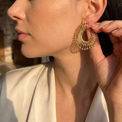 Woman wearing gold hoop earrings with a stone wall background