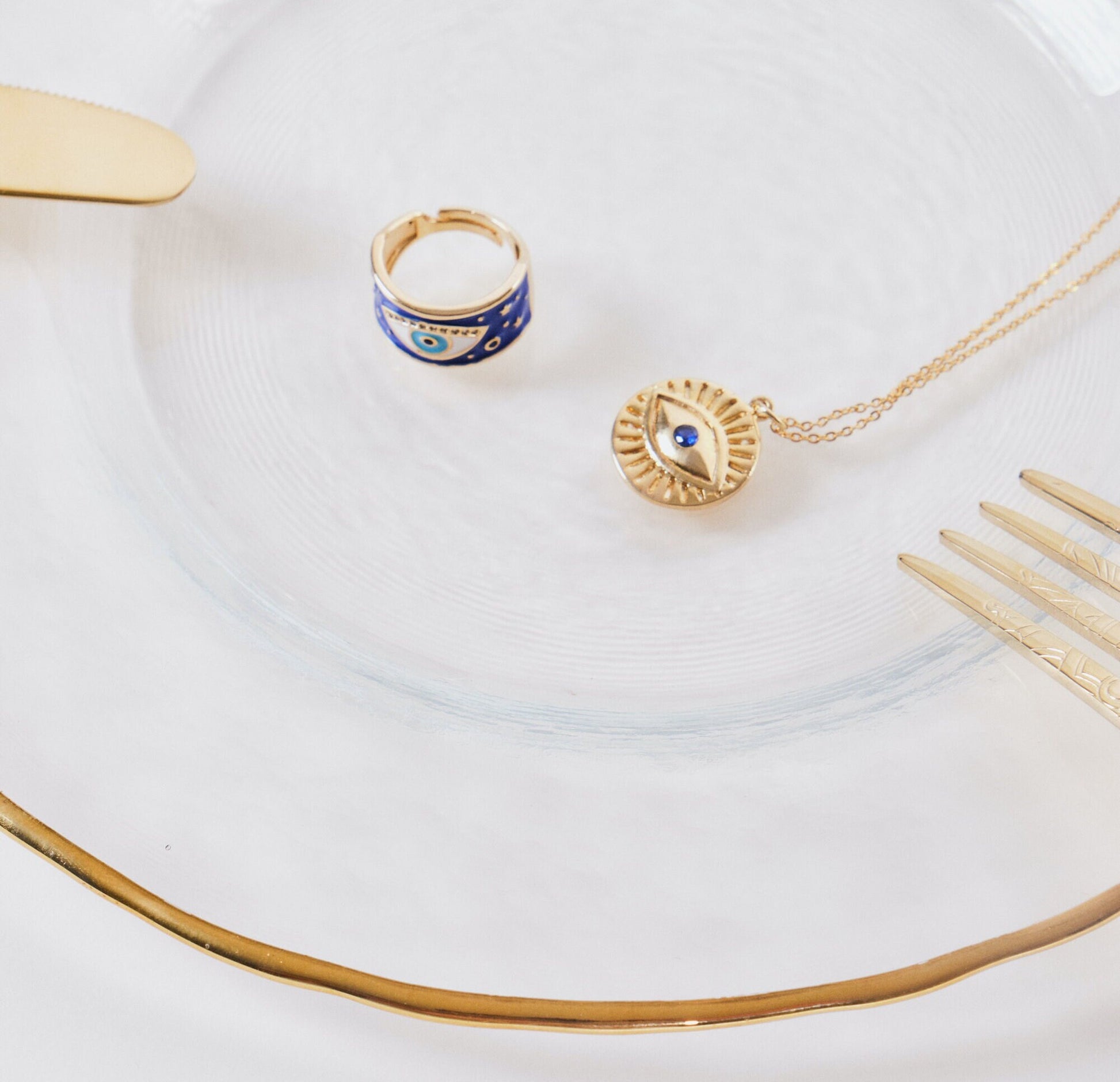 24k gold evil eye ring & evil eye necklace on a golden plate with gold knives & fork