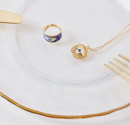 24k gold evil eye ring & evil eye necklace on a golden plate with gold knives & fork